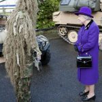 ギリースーツを着てライフルを持った兵士と会話するエリザベス女王